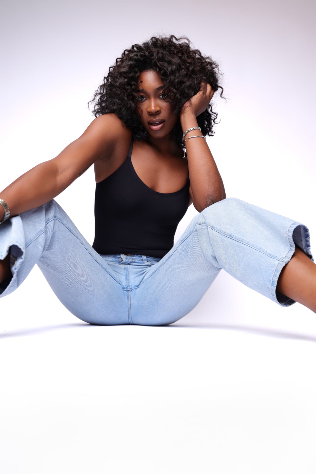 Model with a full head of natural curls seated in soft denim